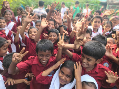 Crowd of schoolchildren on Bangladesh raising their hands and smiling