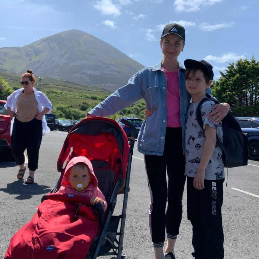 Anya with her son and daughter who is in a pushchair standing in front of a hill 