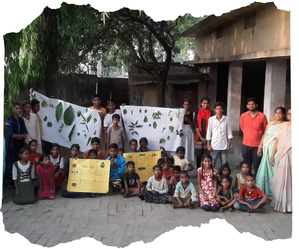 A class of children and their teachers are posed for a photo with some large banners made with leaves and posters celebrating Earth Day