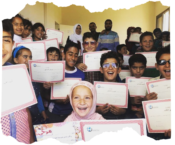 Big group of Syrian refugee students aged between 7-11 smiling and laughing and holding up certificates. 