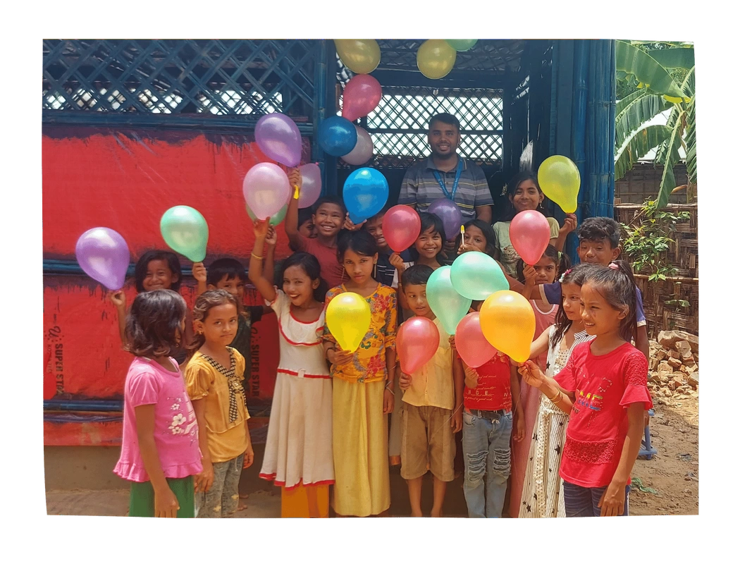 Children outside their classroom in Kutupalong camp are holding up colourful balloons, smiling.