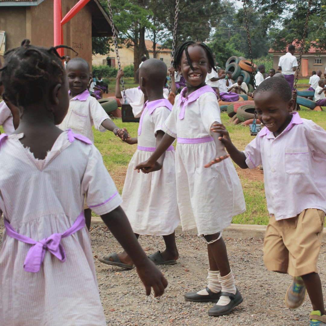 Group of Ugandan children playing outside their school in Loco. They are holding hands in a circle and smiling. You can click on the image to read more about the campaign to end child sacrifice.