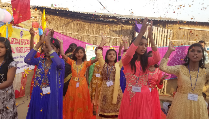 A group of Indian girls wearing bright coloured sari's are dancing together outside in celebration.