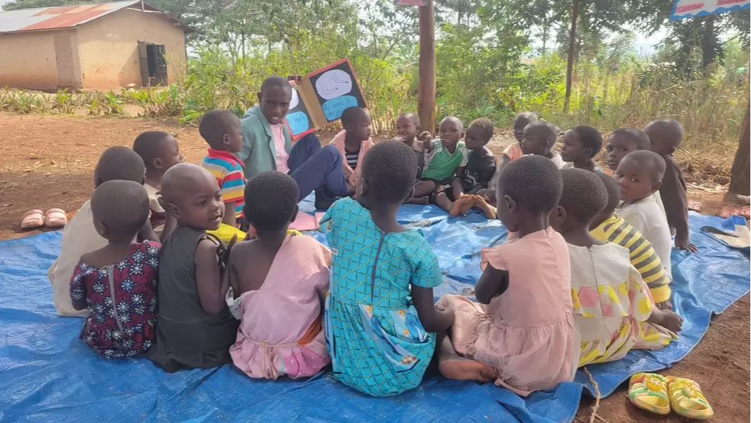 Children in a circle with their teacher during a cluster lesson in Uganda