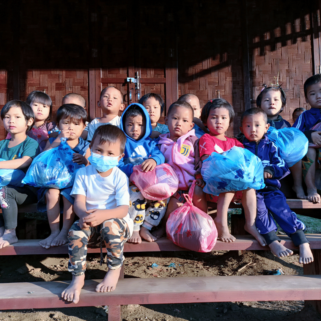 Group of Kachin children from Myanmar sat with bags of warm clothes provided by Children on the Edge
