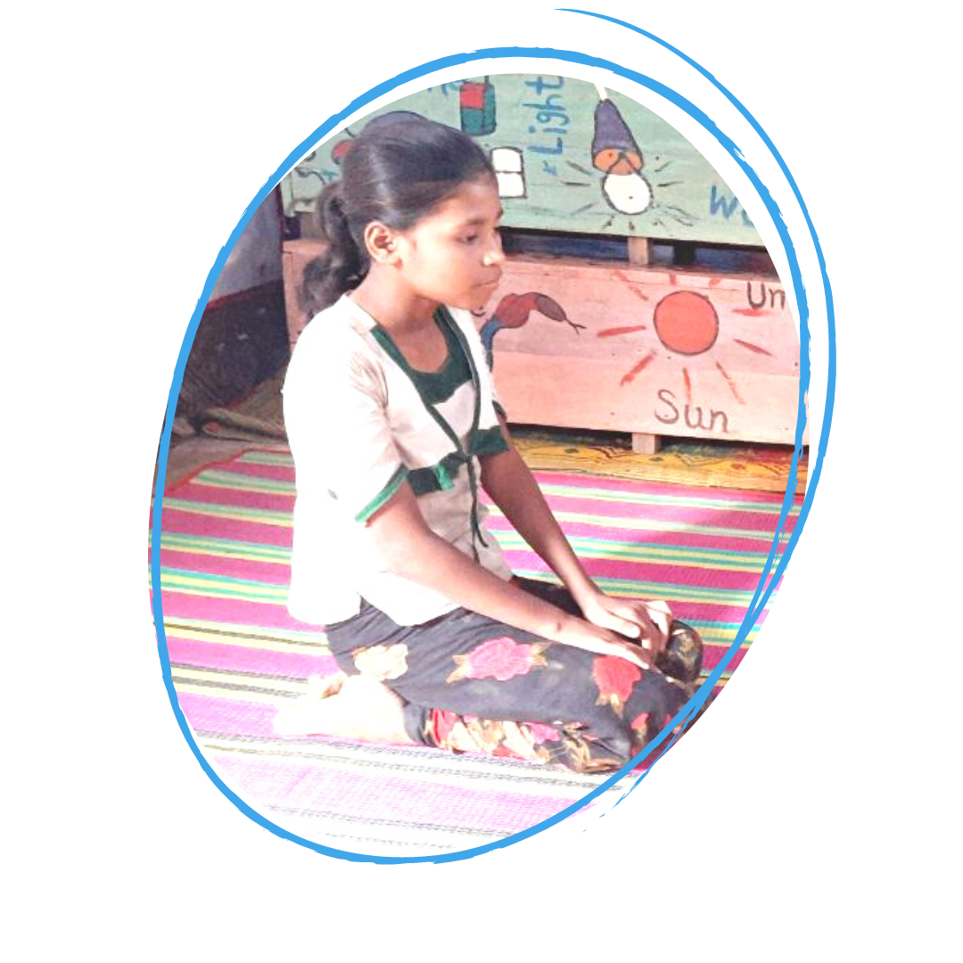 Minara, a 10 year old girl is kneeling down in a bright classroom on a mat.