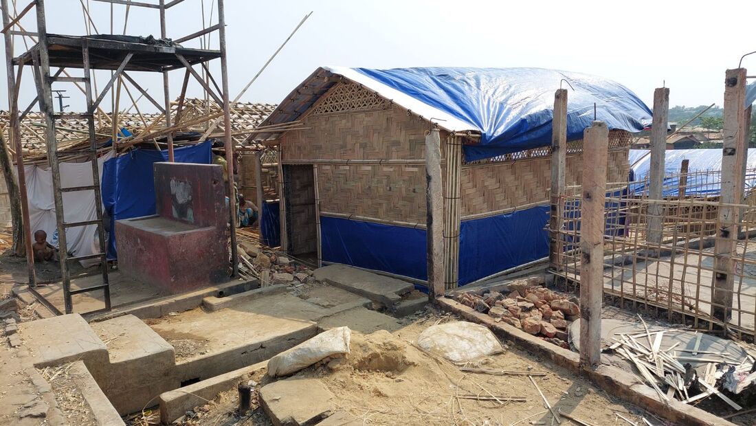 A bamboo structure, with blue tarpaulin is near completion, building materials and scaffolding surround the new classroom