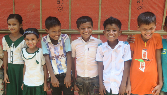 Four Rohingya boys and two girls smiling outside their classroom in Kutupalong camp