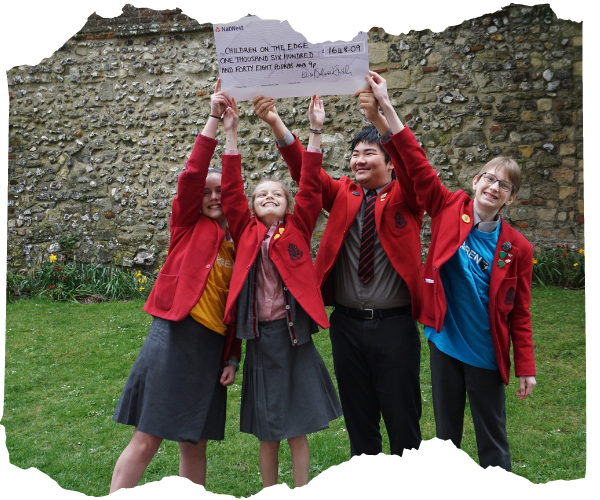 Four schoolchildren in red blazers are stood together outside with their arms in the air 
