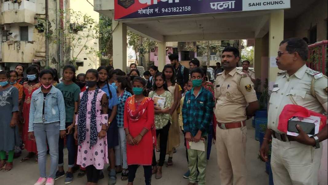A group of Indian teenagers are stood outside an police station in Patna with two uniformed police officers. 