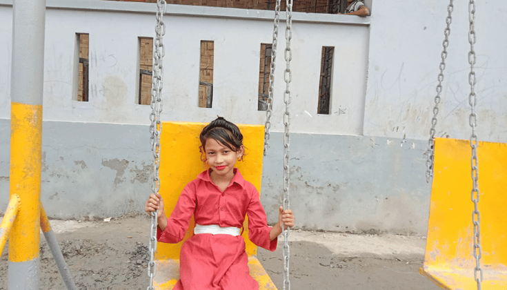 Puri, a young Rohingya girl aged 7 is sitting on a swing 