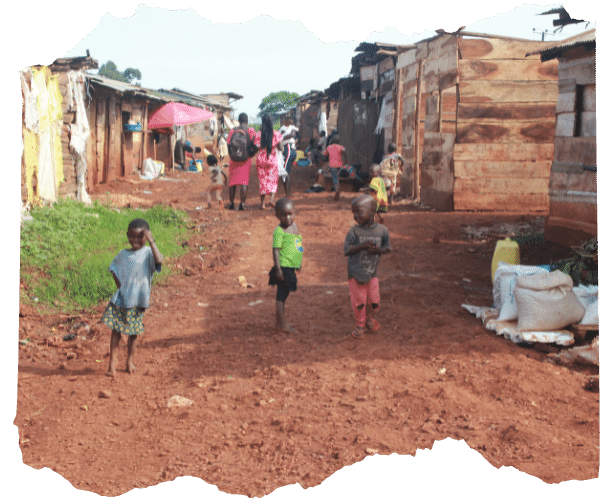 A slum community in Jinja, Uganda showing a muddy street lined with makeshift houses and children playing barefoot outside. 
