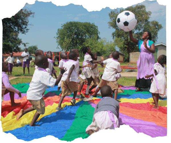 Children playing with a ball on a colourful parachute outside their school in Uganda