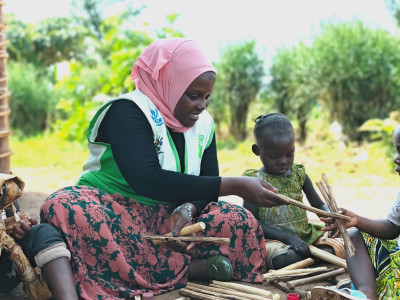 Uganda woman with Children on the Edge tabard plays counting sticks with Congolese children