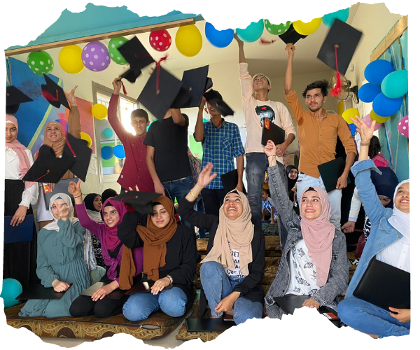Group of Syrian refugee students aged between 15-18 surrounded by balloons, smiling and laughing and throwing graduation caps into the air.