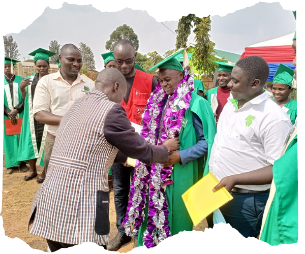A refugee teacher from the DRC is being given his certificate from a district education officer, a man in a smart suit. The graduate is wearing a bright green gown and is stood with a group of fellow graduates in gowns, men and women. 