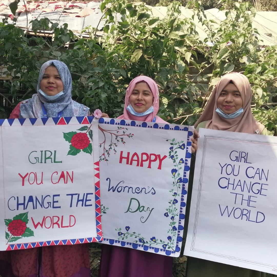 Project officers in Bangladesh holding up international women's day signs saying 'girl, you can change the world'.