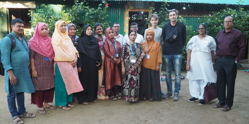 Mukti staff - 11 adults are stood next to John, Veena and Renji outside a community school in Bangladesh