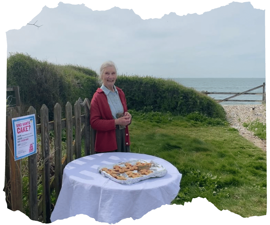  An older woman in a red cardigan standing by a table with cakes on