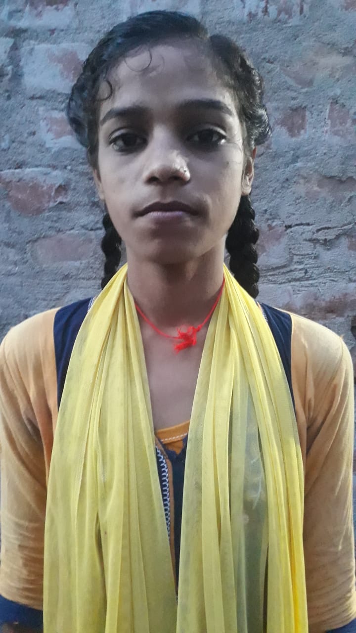 Puja Kumari, a 13 year old Indian girl with dark braided hair and a yellow scarf. She is looking at the camera with a serious face.