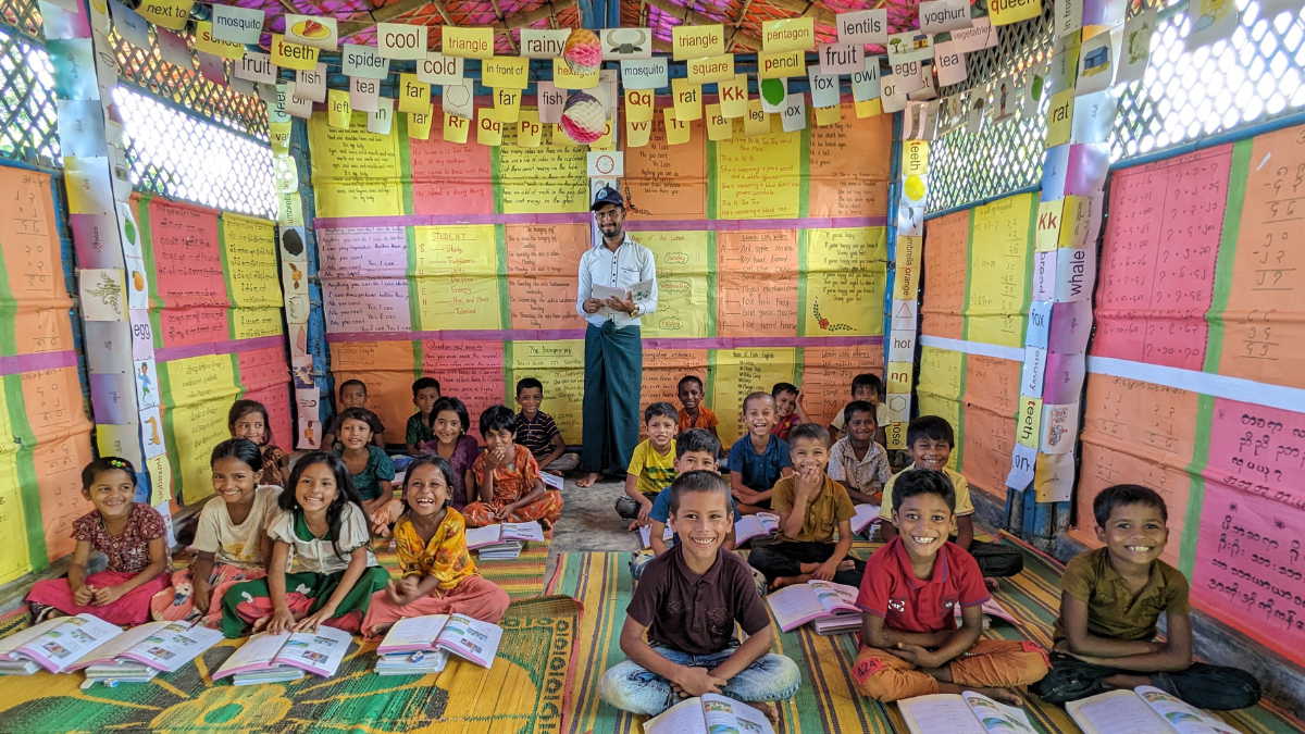 Children in classroom with their teacher smiling at the camera