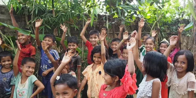 Children in a classroom garden in Kutupalong are raising their hands smiling