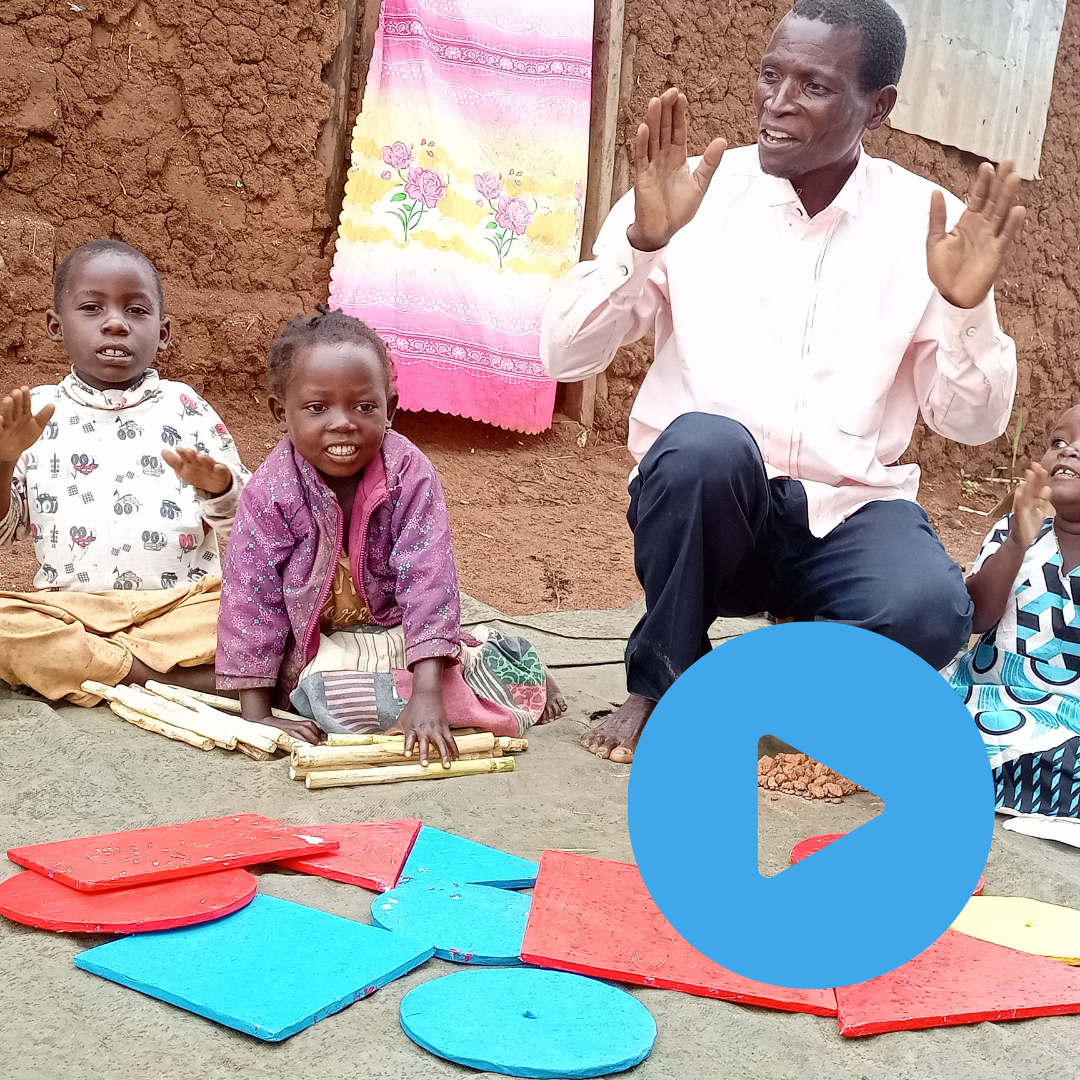 Two young Congolese refugees and their teacher learning outside in Cluster Groups. Click on the image to watch the video.