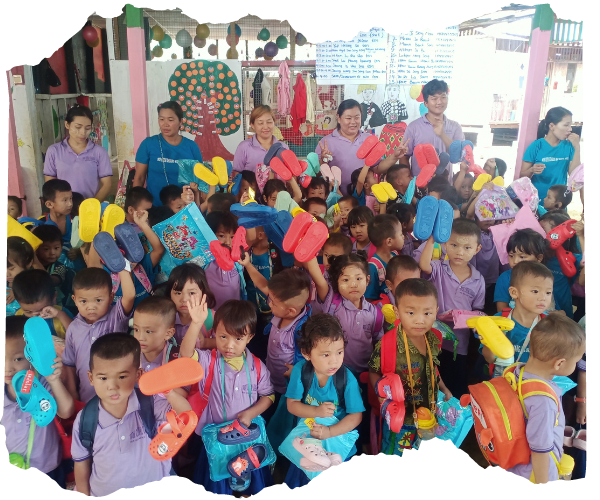 A group on young Kachin children are stood together in class holding up their brand new colourful 'crocs'