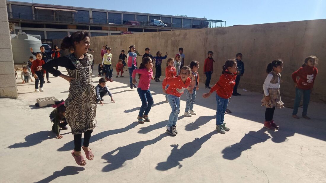 Students in Lebanon taking part in a dance lesson outside their school in the playground. They are jumping and smiling. 