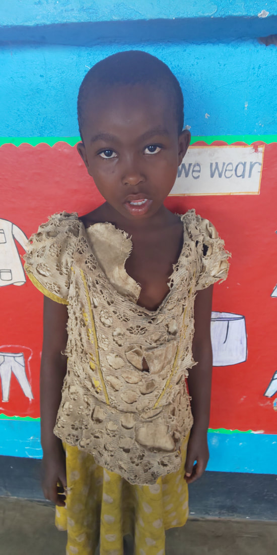 A young Congolese girl, Jante, aged 6 is wearing a yellow dress standing in front of a brightly coirl, Jante, aged 6 is wearing a yellow dress standing in front of a brightly coloured wall in her classroom.