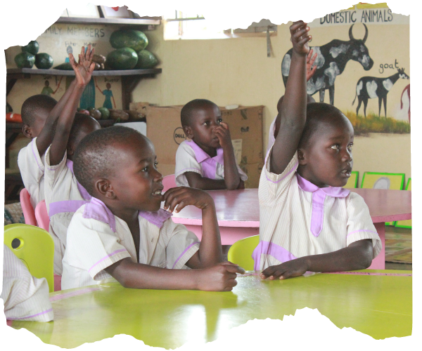 Young children in Uganda are in an Early Childhood Development Centre. They are listening to a lesson and facing a teacher who is off camera. Some are smiling and some have their hands up. They are wearing lilac and white uniforms. 