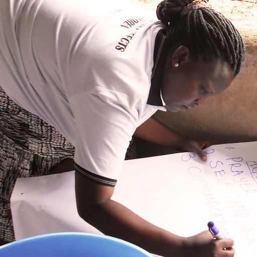 Babra, a black woman  is writing on a large piece of paper, wearing a white tshirt