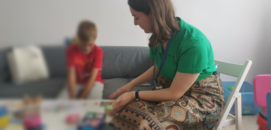 Female therapist does play therapy with child in red tshirt. Child's image is blurred.