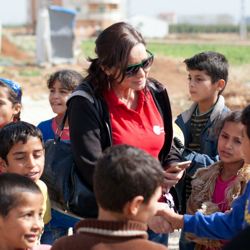 Nuna is wearing sunglasses and a red tshirt and is surrounded by Syrian refugee children as she takes a photo on her phone