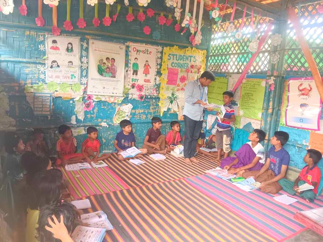 Project Officer Panesh in a colourful learning centre with a class of Rohingya children