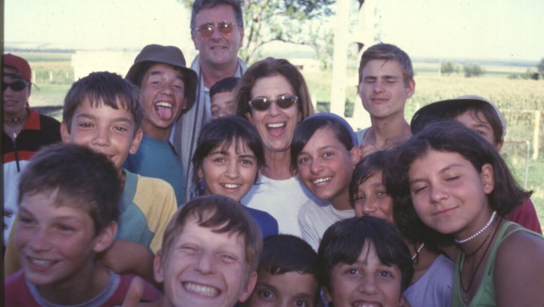 An image from the 1990s with a young Anita Roddick surrounded by smiling teenagers and her husband, Gordon behind her