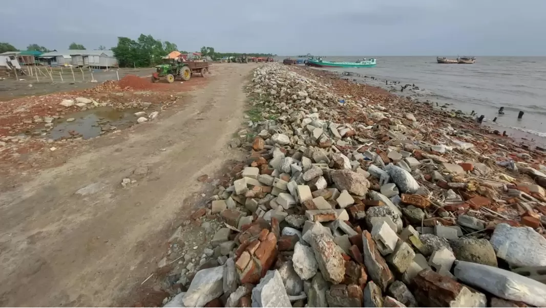 The coastline of Bhasan Char, bricks and rubble border a dirt road next to the sea line