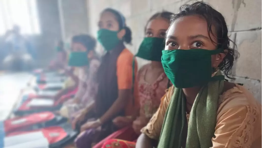 Rohingya children sat against the wall in their classroom, wearing green masks