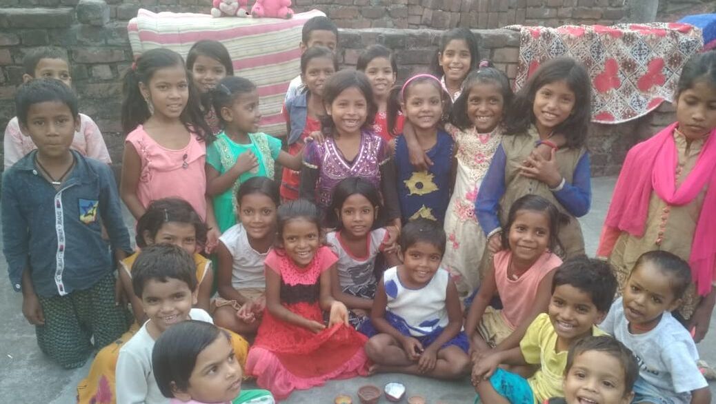 A group of (mostly) girls from a children on the edge learning centre in India are sat together on the floor in a semi circle looking smiling