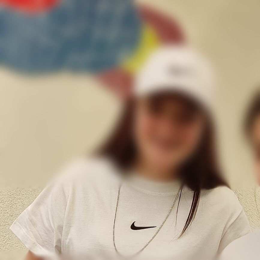 Teenage girl with white Nike Tshirt and Nike cap smiling, face blurred. 