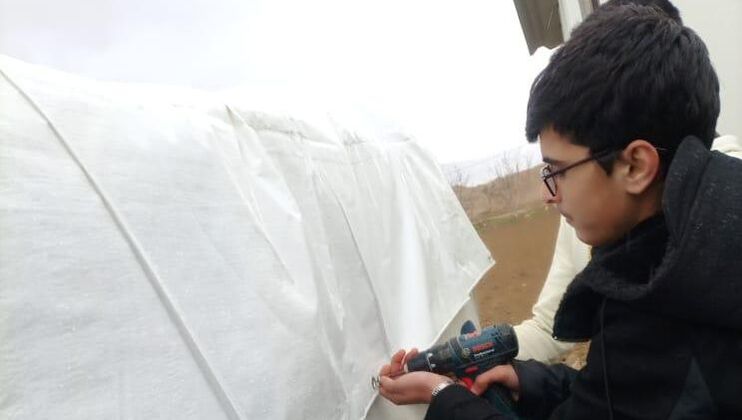 Student, Mahmoud weatherproofing a refugee tent with a new tarp