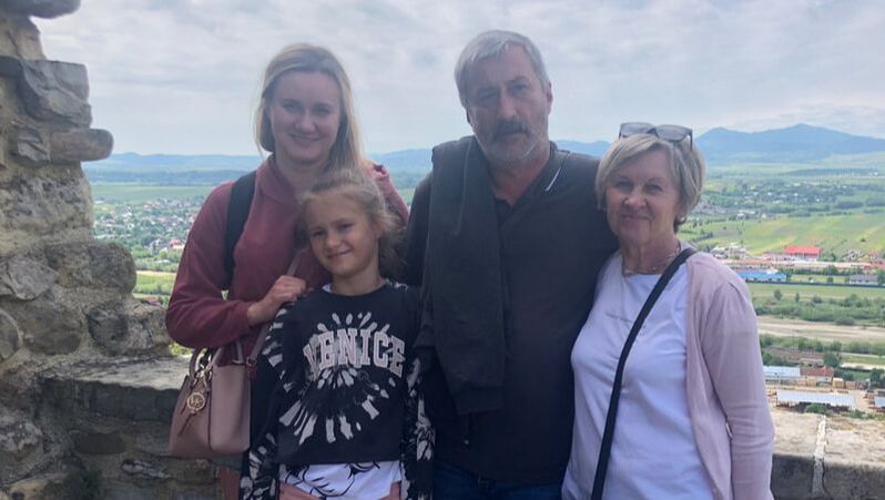 Iryna stands at a tourist spot with her daughter and parents, they are all smiling. 
