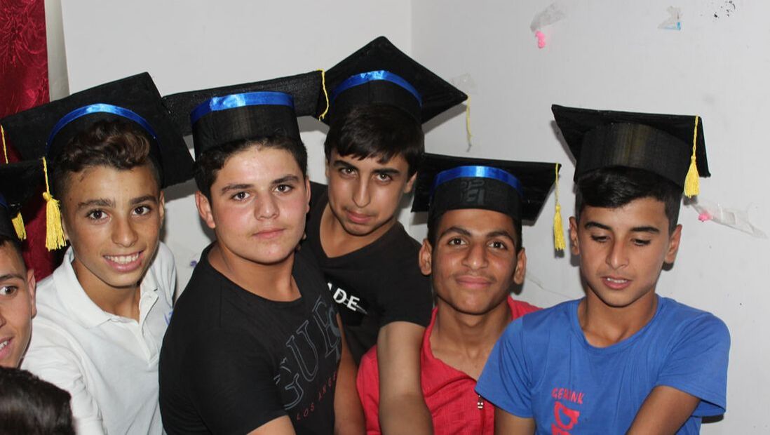 Five Syrian teenage boys wearing graduation hats. They are smiling to celebrate passing their Syrian high school exams.