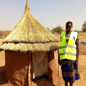 Maria standing in front of the pit latrine that she built herself