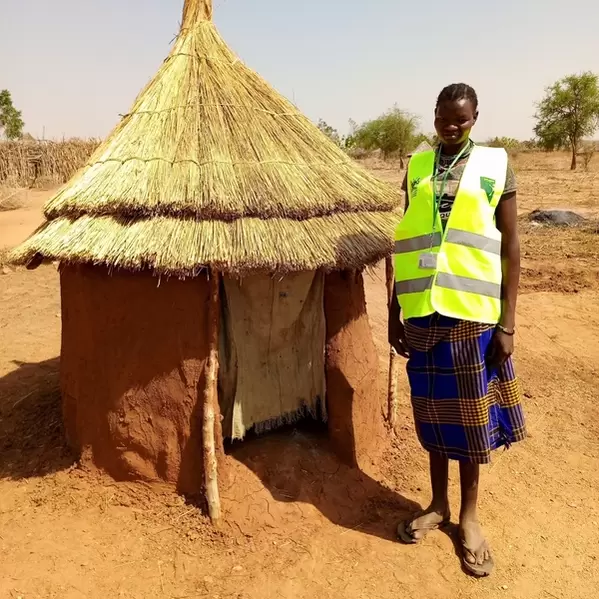 Maria, a child protection team member standing outside the latrine she built in her home in Karamoja