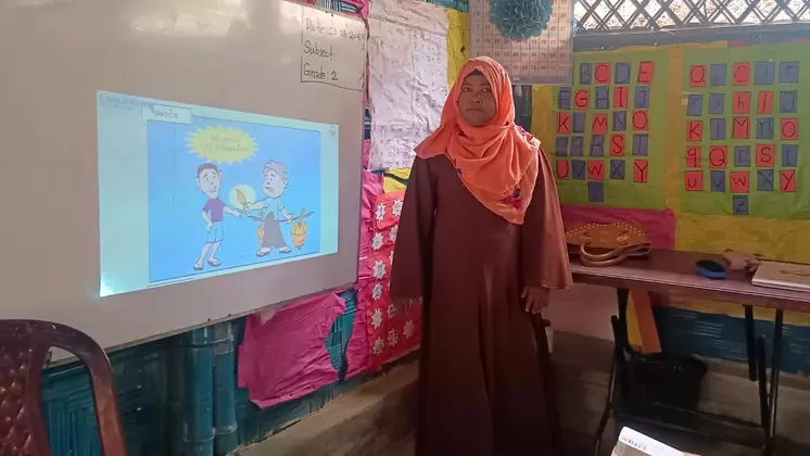 A teacher standing next to the screen which is showing a lesson