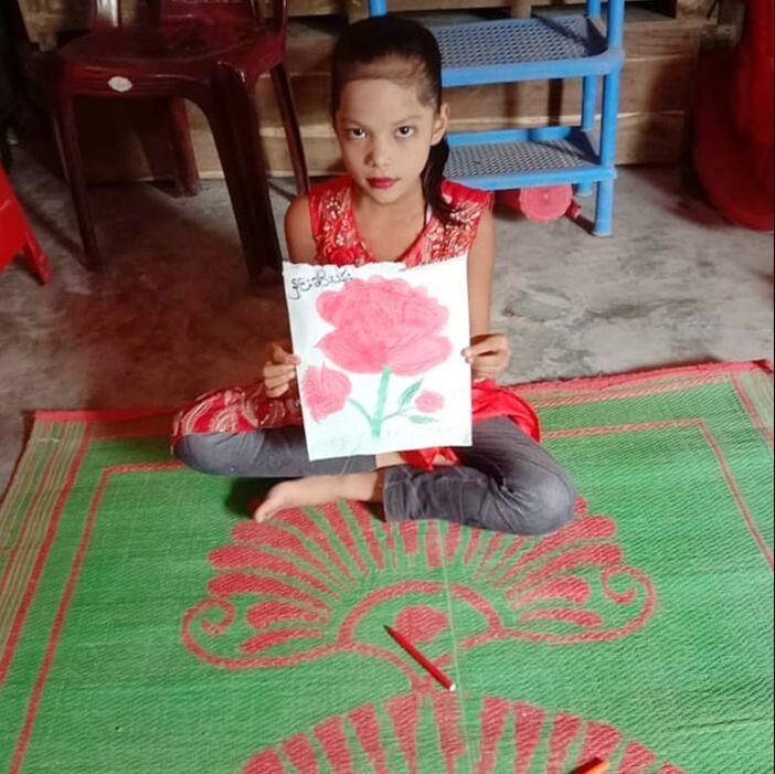 Yasmin sat on a green mat inside her classroom holding a hand painted picture of a flower
