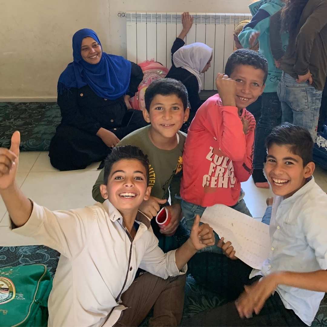 Group of Syrian refugee boys laughing and giving the camera a 'thumbs up' as they sit in their classroom in Lebanon. 