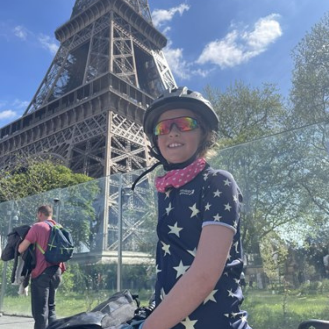 Nine year old Florence in her cycling gear, with her bike standing at the foot of the Eiffel Tower in Paris on a sunny day
