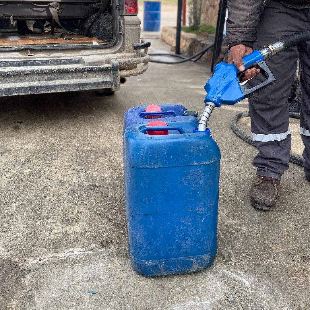 Blue jerry can being filled up by hand with fuel from a petrol pump